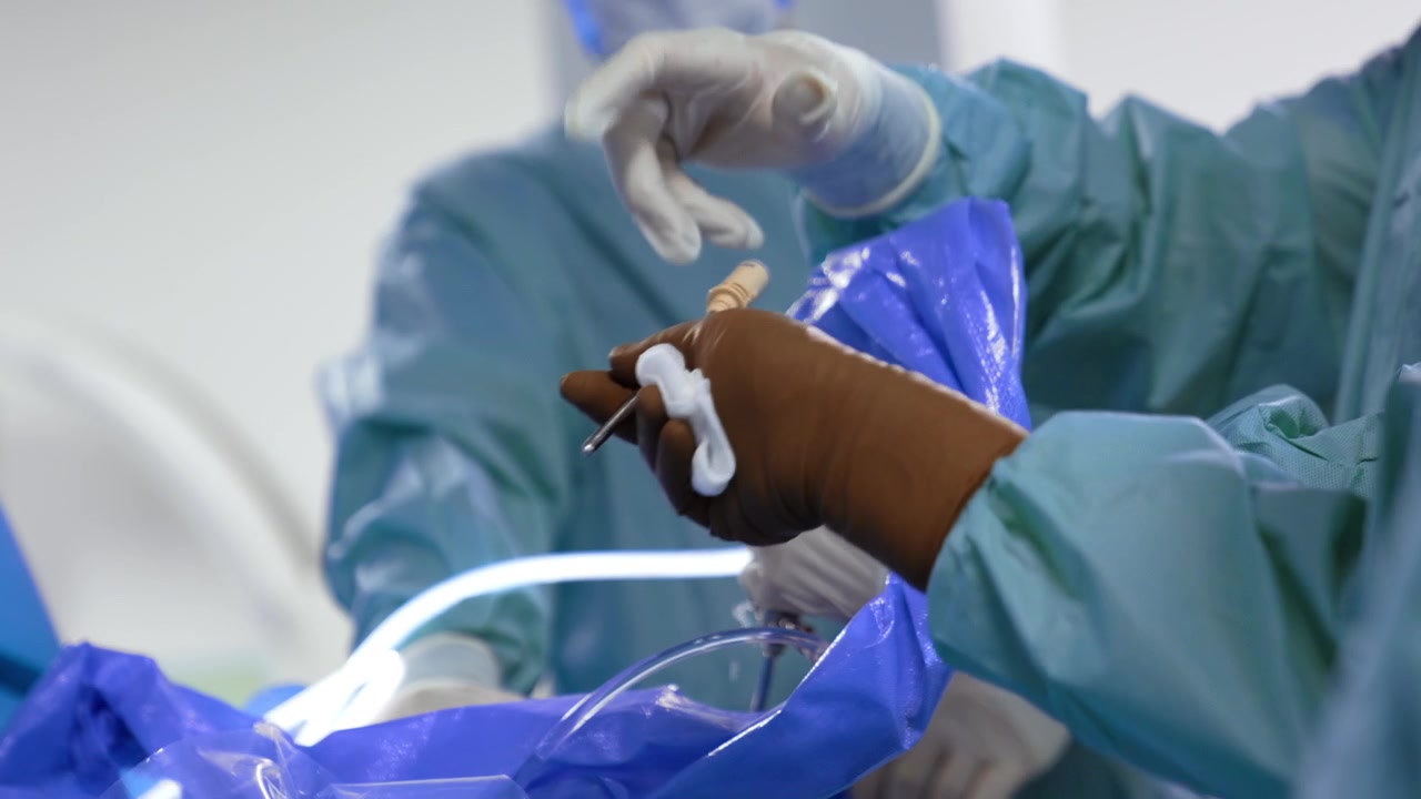 Unrecognized surgeon using the surgical device at operation. Some water splashes from the instrument. Assistant passes the tool to the chief doctor.
