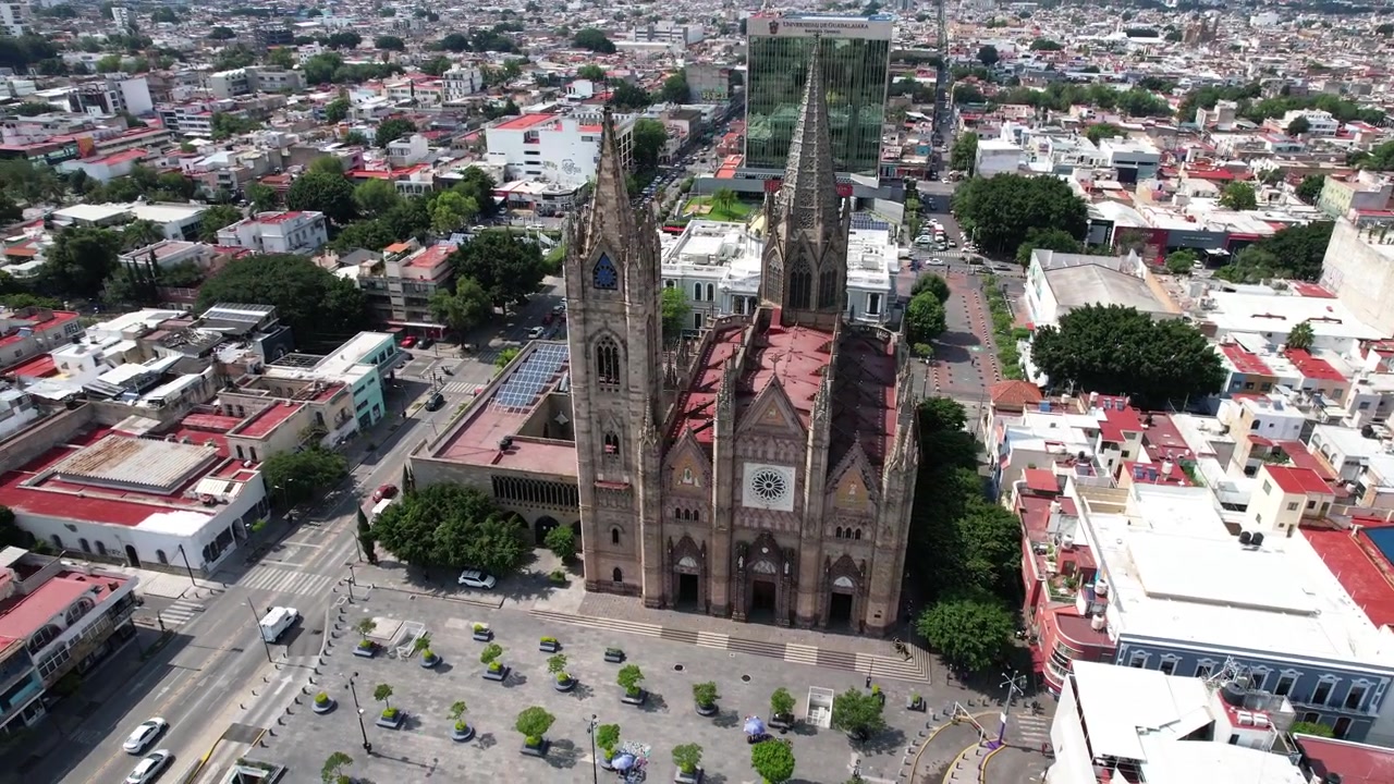 Órbita cinematográfica de drone em torno de uma histórica igreja gótica, exibindo sua arquitetura e a paisagem urbana circundante em Guadalajara.