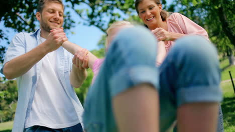 two parents smile as they swing their daughter back and forth by his arms playfully