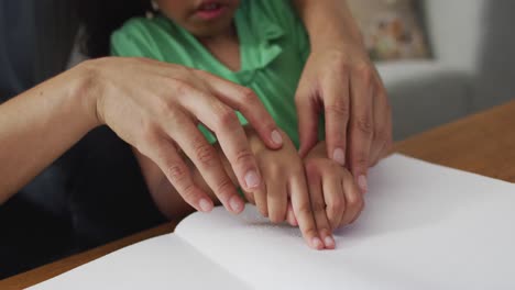 happy biracial father and daughter sitting on sofa reading braille