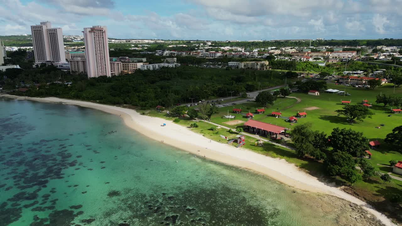 Aerial flyover of vibrant ocean coastline and white sand beach along Ypao Public Park with lush greenery and turquoise waters at Guam, USA