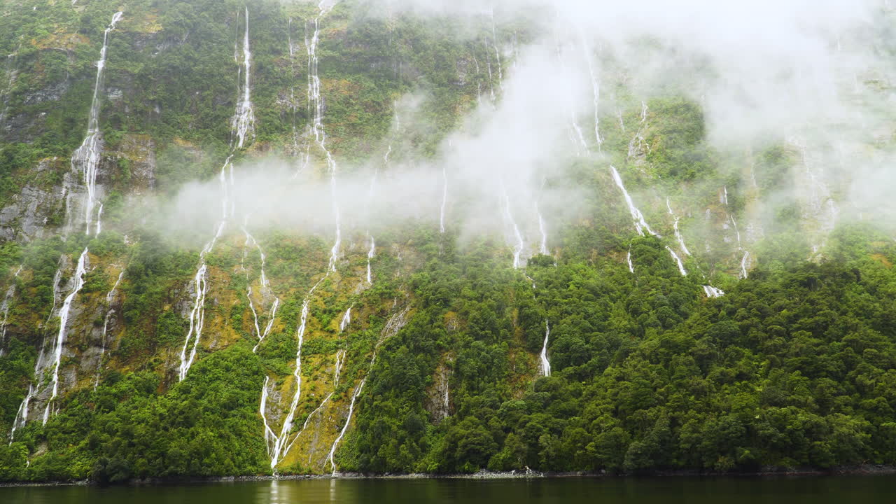 Cascade waterfalls flowing from cliff in milford sound, over mist evaporating from rain forest