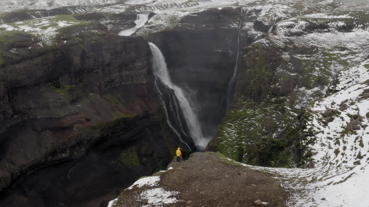 antena: paso elevado de una persona con chaqueta amarilla, mirando la cascada granni en islandia