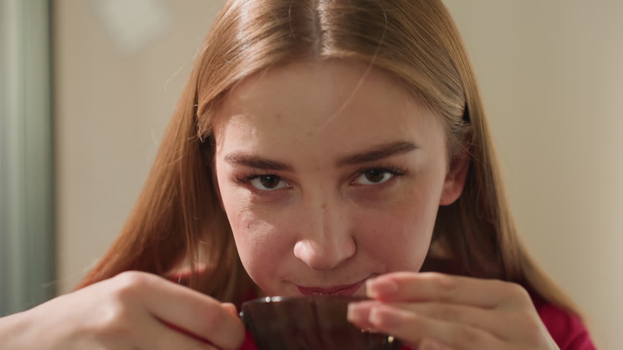 편안한 여성이 평온한 순간을 즐기고 있어요. 아늑한 주방에서 학생이 부드러운 아침 차를 마시며 잠시 휴식을 취하고 있고, 햇빛이 드는 아늑한 주방에서 밝은 피부의 젊은 여성이 차분하게 차를 마시고 있네요.