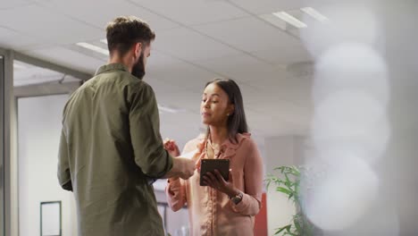 Video-of-diverse-businesswoman-and-businessman-using-tablet-and-talking-in-office