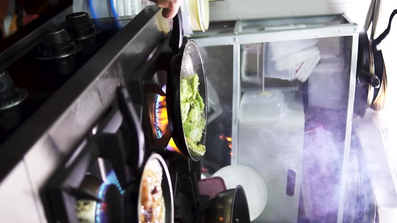 toma manual en cámara lenta vertical de salteados deliciosos trozos de aguacate arremolinados en una sartén negra sobre una estufa de gas en una elegante cocina de restaurante