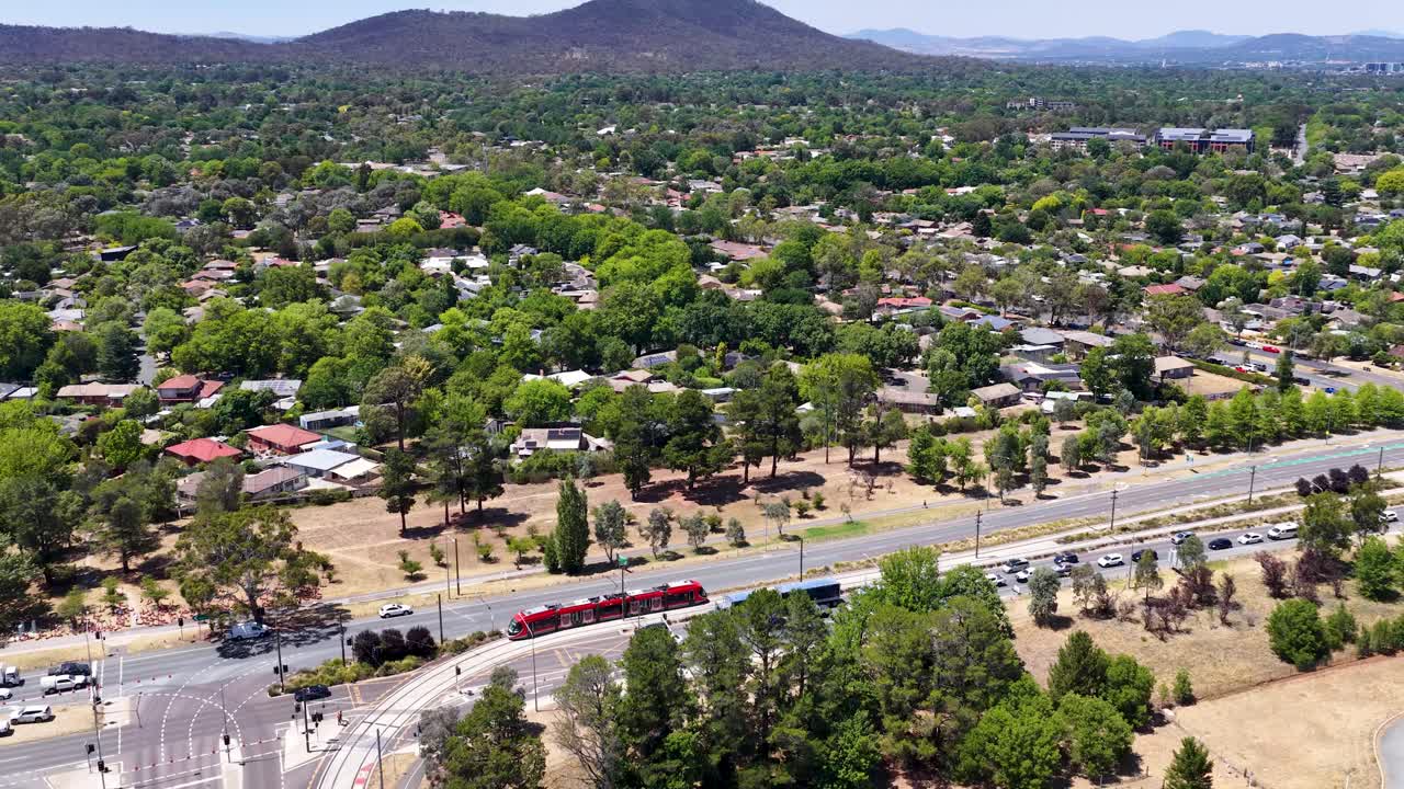 Ripresa aerea dall’alto con drone che segue un tram rosso che si muove attraverso paesaggi suburbani verdi in Australia