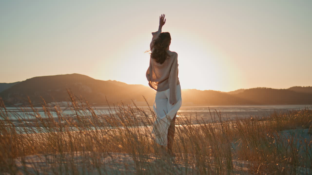 Woman watching sunset light with clothing swaying on wind. Happy brunette