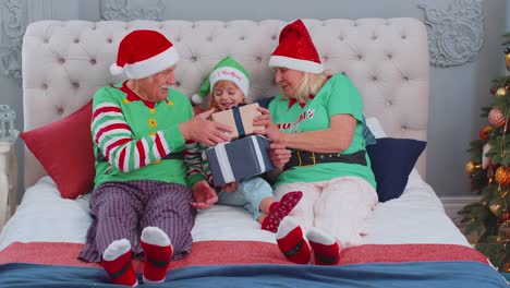Senior-grandparents-with-granddaughter-girl-kid-exhcanging-gifts-at-home-bedroom-near-Christmas-tree