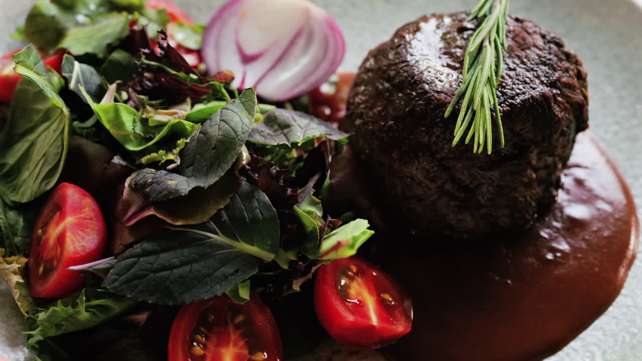 Close up of a filet mignon with a red wine sauce and a fresh salad garnish