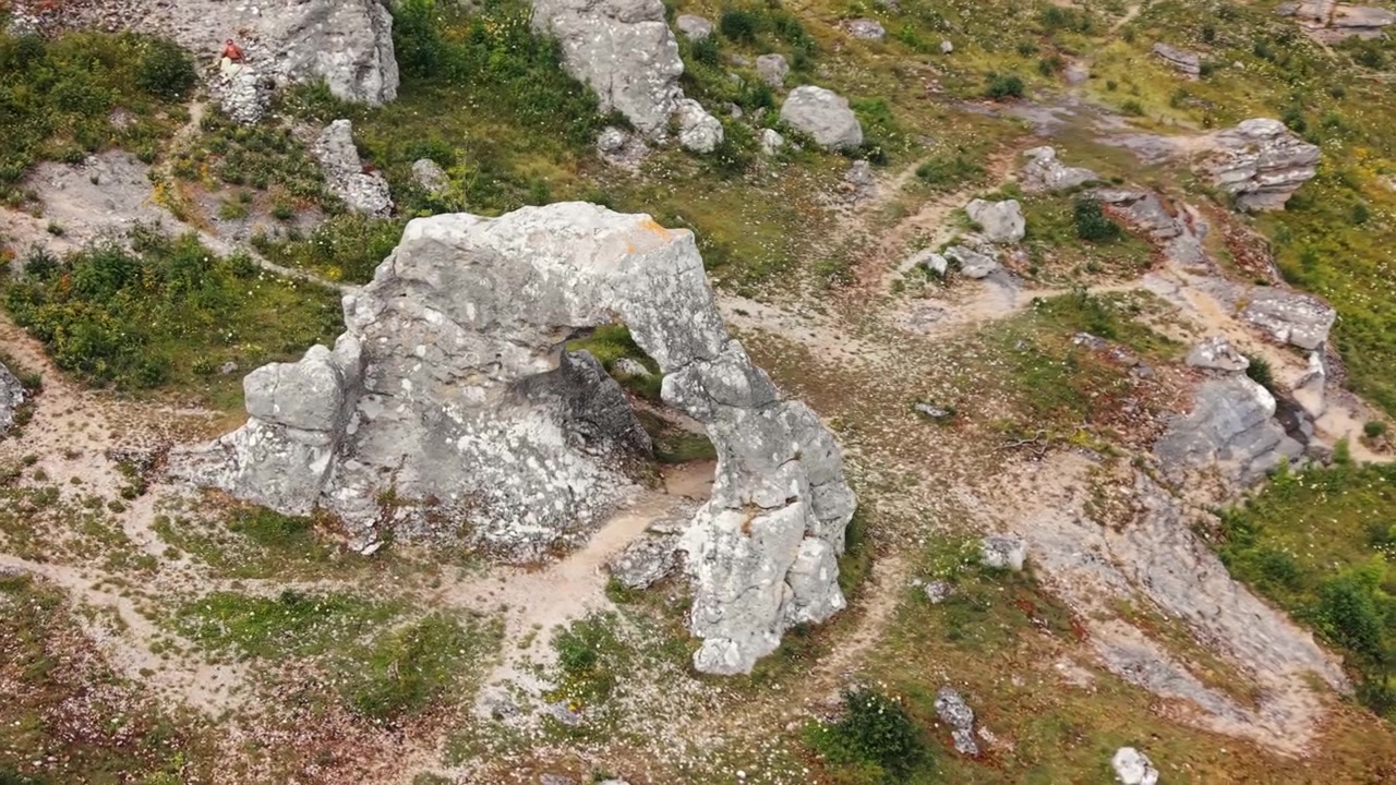 Vista aerea di raukar calcarei erosi e un arco di roccia naturale a Lergrav, Gotland, che rivela una geologia modellata dall'erosione, sentieri e vegetazione rada.
