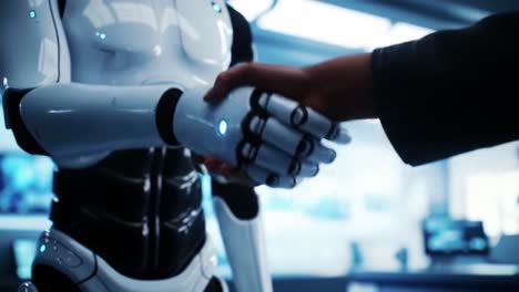 A person extends their hand to shake hands with a humanoid robot in an innovation laboratory. The environment is filled with advanced technology, showcasing human-robot interaction.