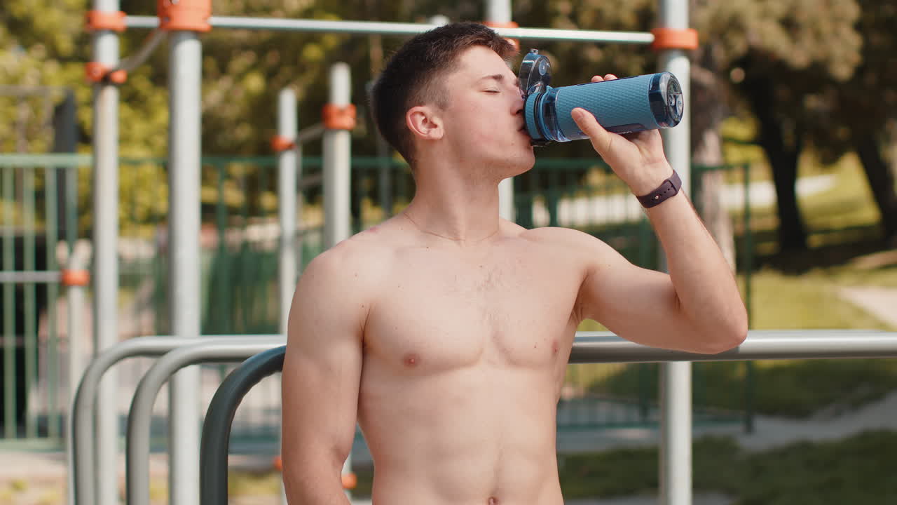 Dehydrated thirsty athletic runner muscular shirtless man drinking water from bottle after jogging