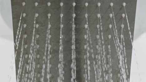 Closeup-shot-shower-jet-water-drops-falling-at-white-grey-bathroom-opening-flow