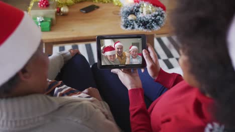 African-american-mother-and-daughter-using-tablet-for-christmas-video-call-with-family-on-screen