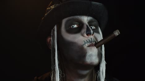 sinister man with horrible halloween skeleton makeup smoking cigar, making faces, smiling, laughing