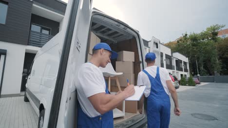 two young workers of removal company are loading boxes and furniture into a minibus