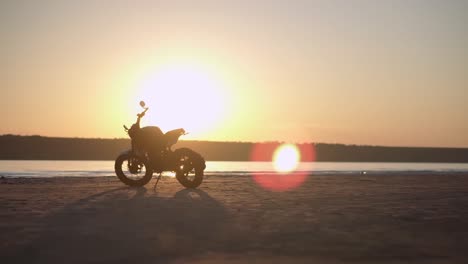 a motorcycle parking on the ground close to the water in sunset with water line on the background. low angle view