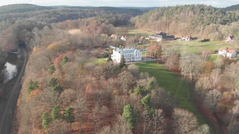 Aerial-view-over-autumn-forest,-flying-towards-grand-country-houses