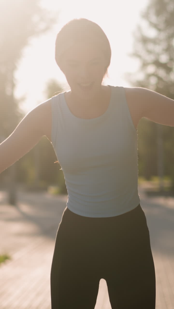 joven mujer sonriendo mientras patina al aire libre con las manos abiertas para el equilibrio, la luz del sol se refleja en ella creando un brillo brillante, y el fondo borroso de vegetación exuberante, árboles y paisajes de parques naturales