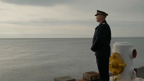 a man in uniform stands on a pier looking out at the sea