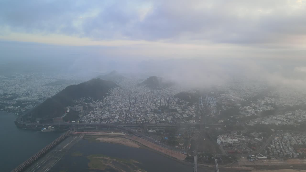 High-altitude aerial drone shot of Vijayawada in the morning, with the city below and the sun rising above the clouds.