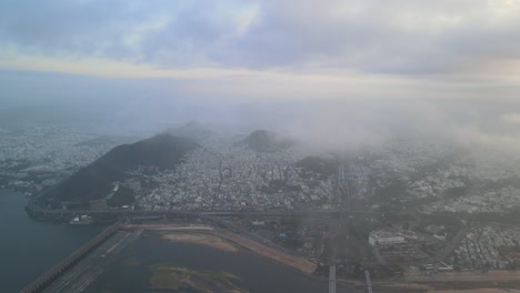 high-altitude aerial drone shot of vijayawada in the morning, with the city below and the sun rising above the clouds.