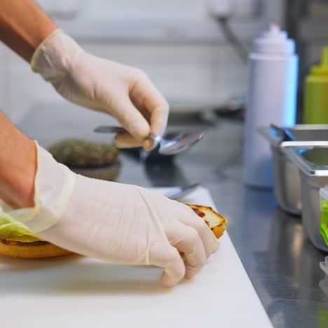 cook adding ketchup on burger. preparing burger on kitchen. cook hands in white gloves preparing and making hamburger. selective focus