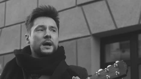 blanco y negro y vista de cerca de un hombre con abrigo cantando y tocando la guitarra en la calle