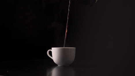 Pouring-Hot-Black-Coffee-Into-White-Cup-From-Glass-Kettle-In-Black-Background