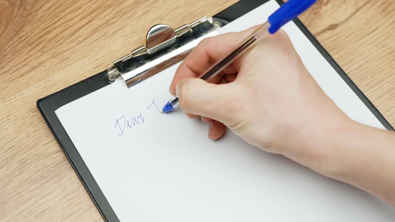 Person writes love note to Valentine on paper, close up view