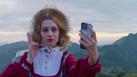 woman poses to take selfie at top of mountain overlook wearing european mountain village dress