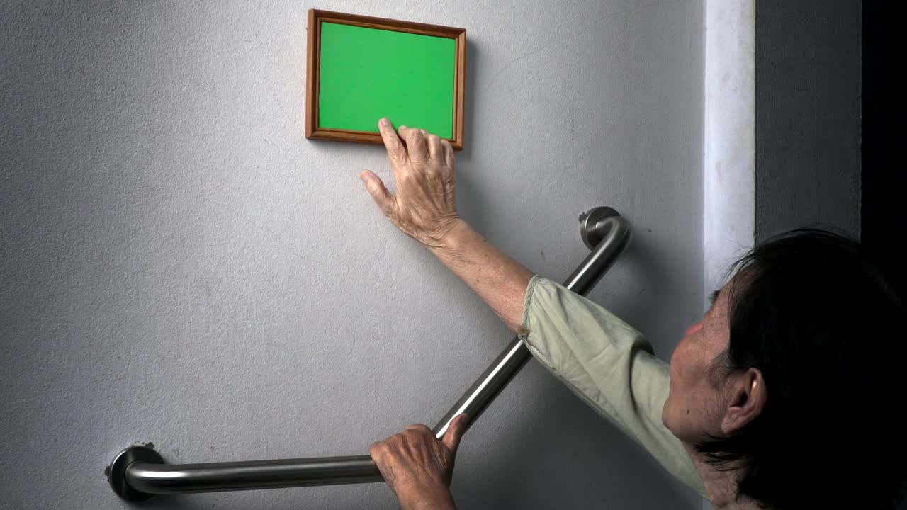 Elderly woman looking at a memories photo on wall , (green screen)