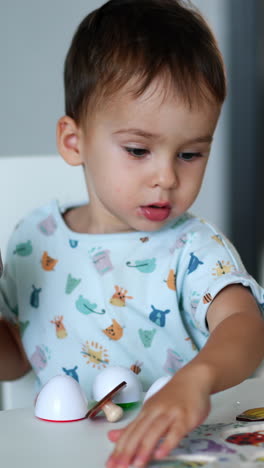 beautiful toddler sitting at desk looking at toys. kid drinks juice from a doypack. blurred backdrop. vertical video