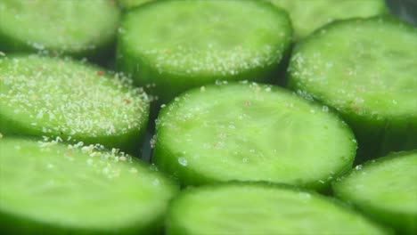 a macro close up shot, falling white garlic grains on a cut slices of a fresh green cucumber, slow motion 4k video