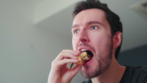 young caucasian man bites into burger at home, cheeseburger eating enjoyment, close up portrait fast food eating, unhealthy eating concept obesity