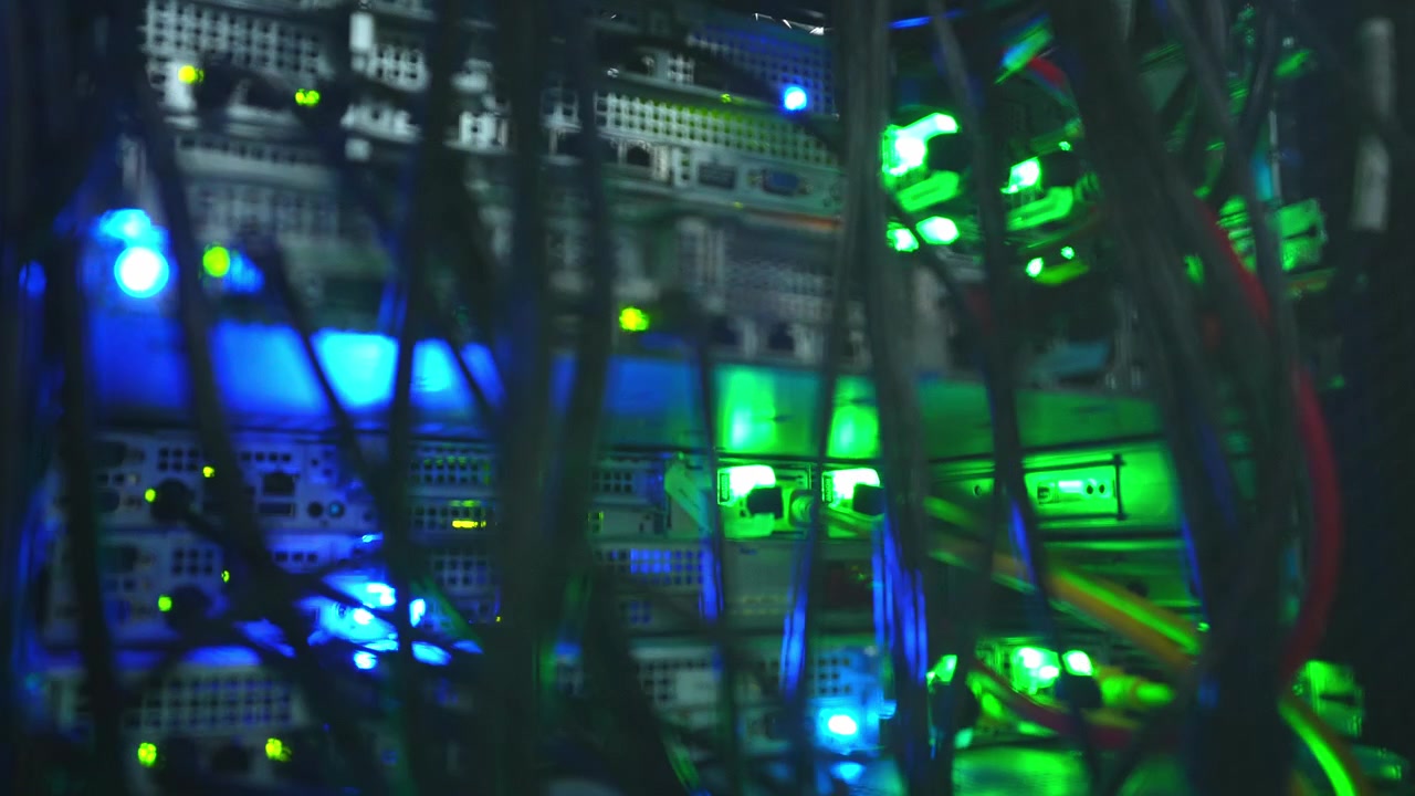 Close-up reveal of dark data center server racks filled with dense cable bundles and glowing blue and green LED indicator lights on active network hardware