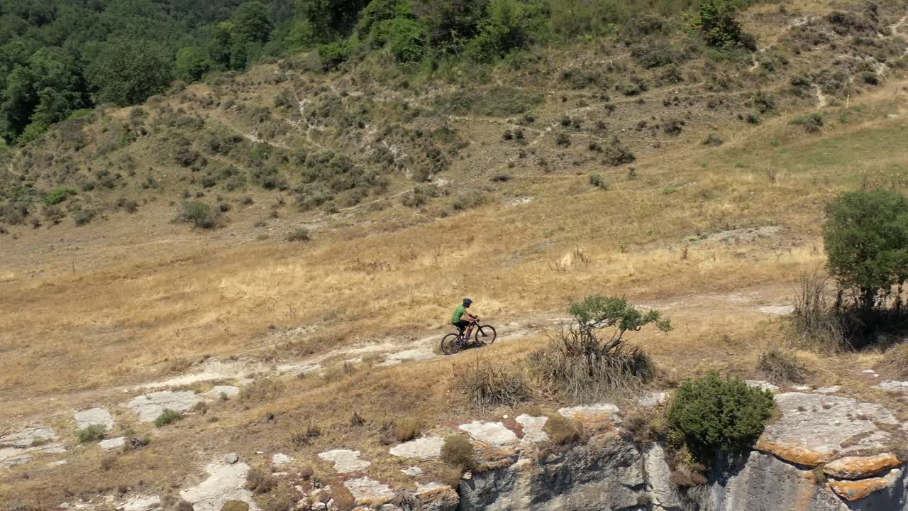 toma aérea lateral de un ciclista de montaña en un paisaje dorado empujando fuerte subiendo la colina