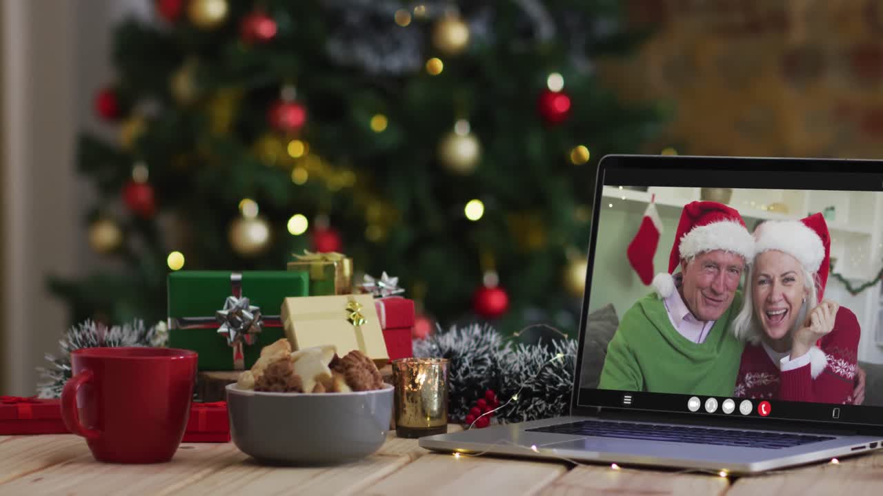 una pareja de alto nivel caucásica saludando en una videollamada en una computadora portátil, con un árbol de navidad