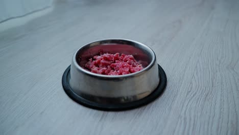 raw ground meat prepared in shiny steel bowl on bright wooden home flooring
