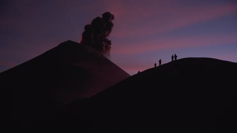 silhouetted group of people witnesses massive lava eruption on ridge of fuego volcano during vibrant twilight