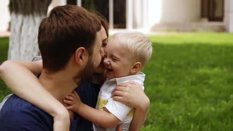 familia feliz y sonriente. madre, padre, hijo pequeño se abrazan. madre besando al niño pequeño y a su marido. pareja feliz. parque verde. cámara lenta
