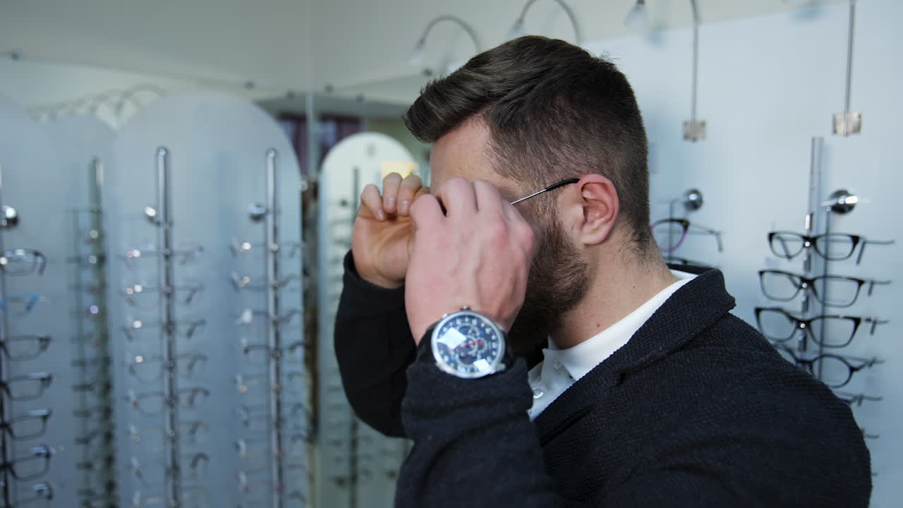 Man choosing glasses at optical store. Young man in optical store trying eyeglasses