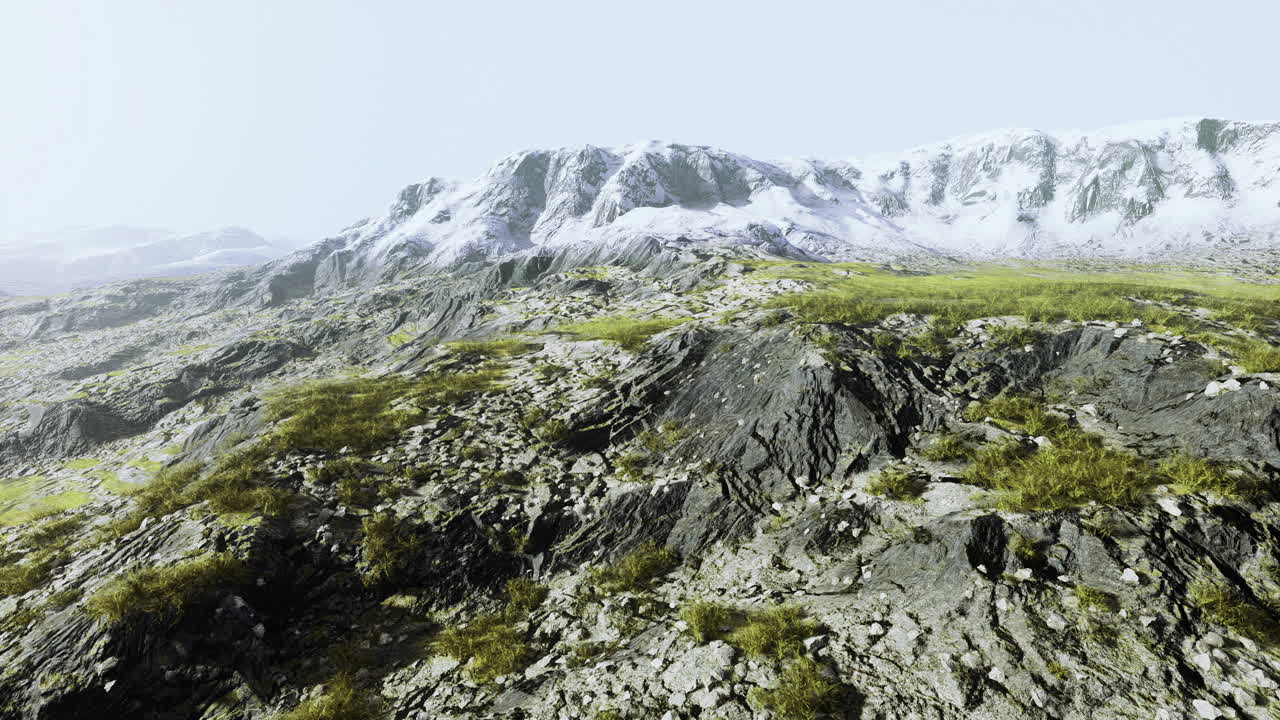 terreno rocoso con parches de hierba cerca de las montañas cubiertas de nieve al amanecer