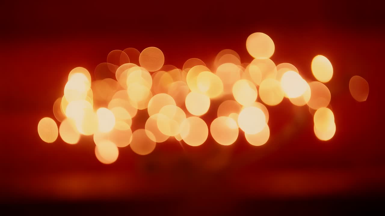 Shifting focus causing centered warm bokeh cluster shimmering and reshaping on deep red backdrop