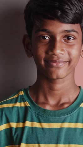 young indian boy, wearing a green and yellow striped t shirt, against a two toned backdrop, his calm demeanor shifting through a series of subtle facial expressions