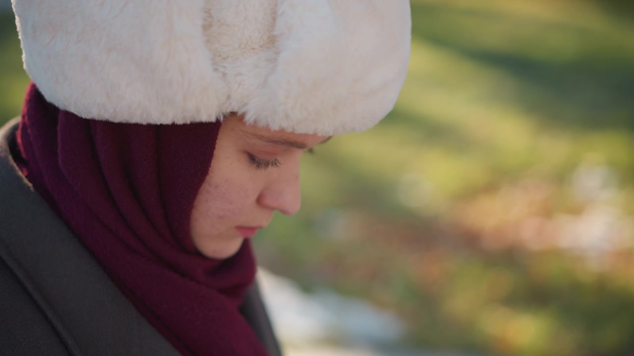 Giovane donna con hijab e cappello di pelliccia che guarda in basso all'aperto.