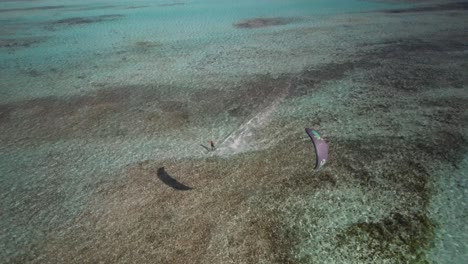 A-kite-surfer-gliding-towards-the-camera-over-clear-waters,-aerial-view