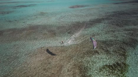 a kite surfer gliding towards the camera over clear waters, aerial view