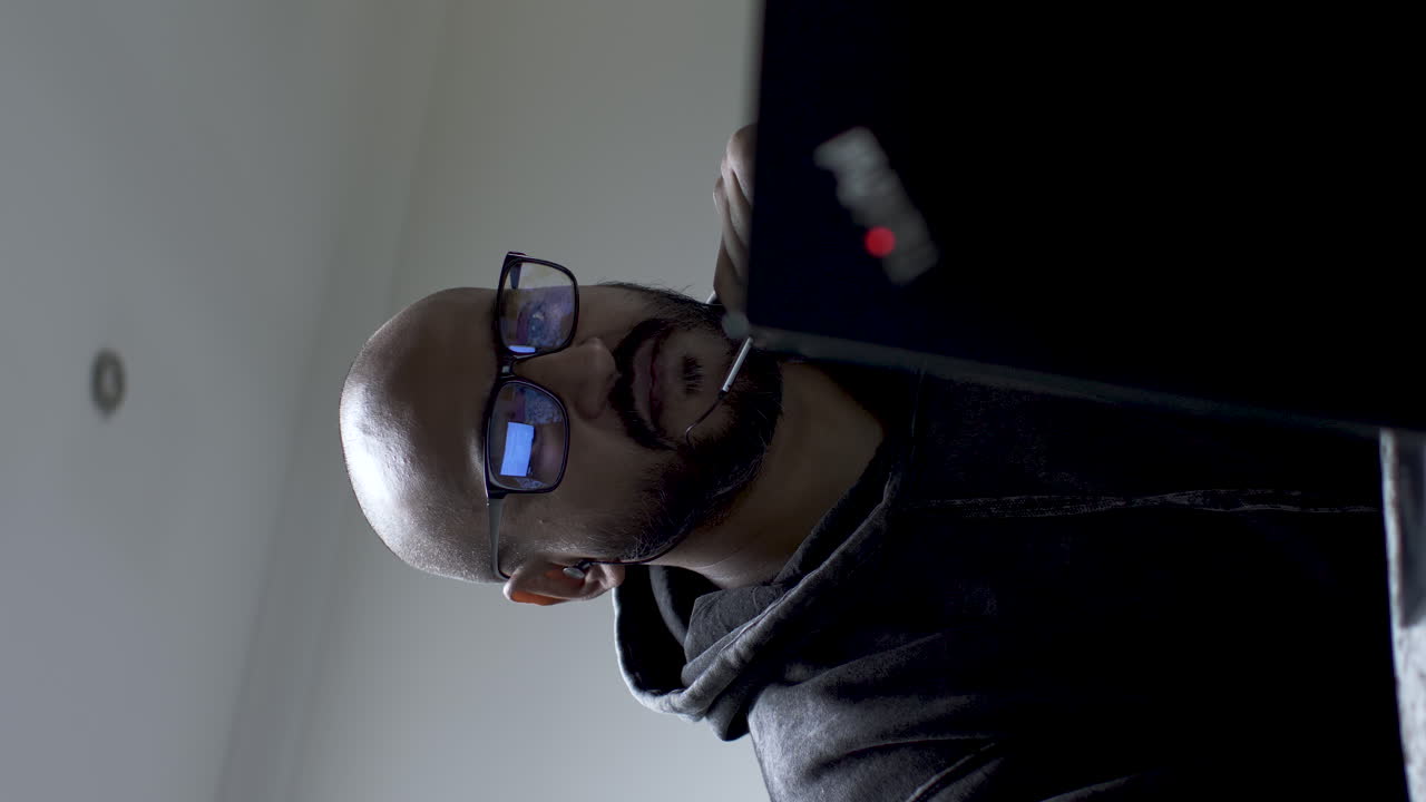 toma vertical de un joven hombre de negocios calvo asiático con auriculares que tiene una conferencia en línea en una computadora portátil en casa